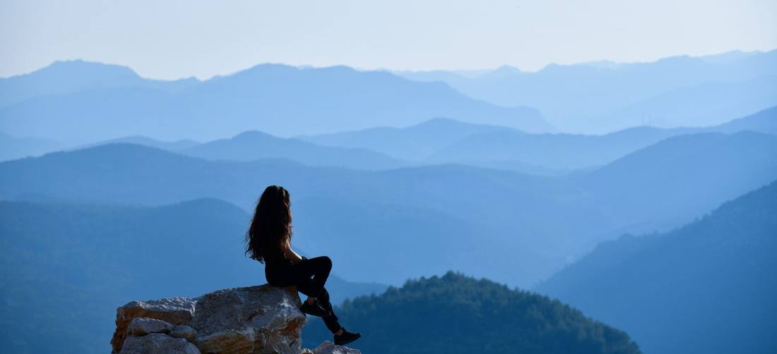 Mujer sentada en una roca, contemplando cordilleras azules envueltas en bruma